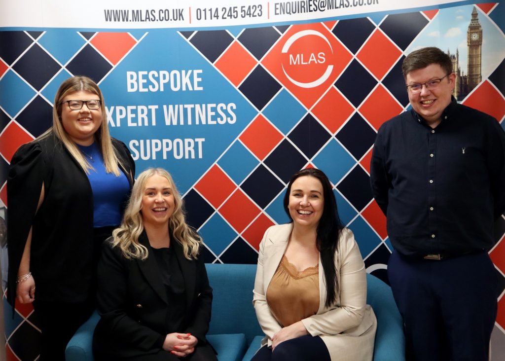 The MLAS Team Leaders sit smiling on a blue sofa in front of an MLAS banner reading 'Bespoke Expert Witness Support'